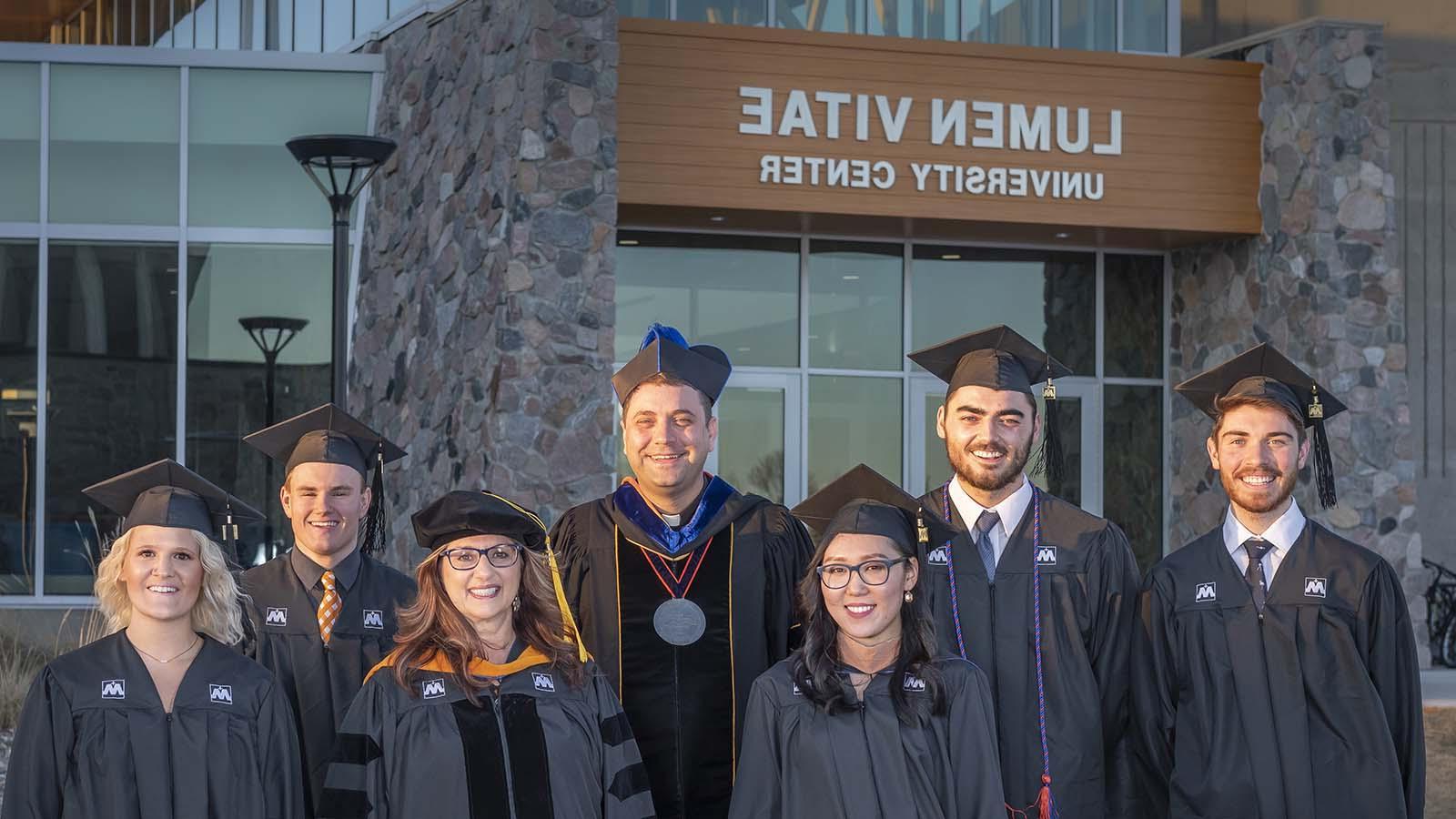 University of Mary graduates standing outside the Lumen Vitae University Center with President Monsignor James Shea.